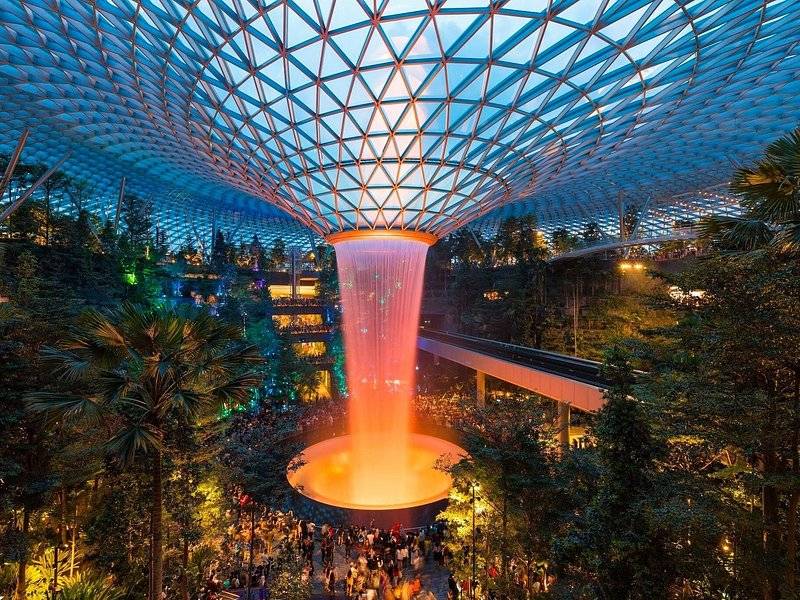 The Rain Vortex falling through the glass dome at Jewel Changi Airport, lit orange at night