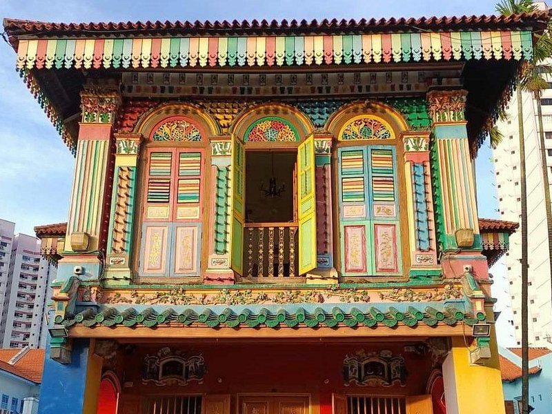 A painted Peranakan shophouse facade with carved timber shutters in jade, coral and gold